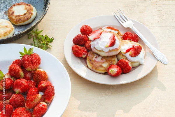 Fototapeta Cheesecakes with strawberries and sour cream. Breakfast in nature. Traditional Russian and Ukrainian dish.