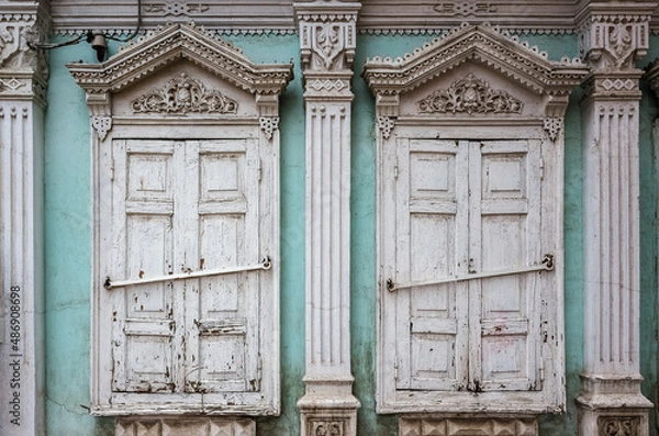 Obraz Two windows with closed shutters of an old house with carved decor and stucco, a fragment of the facade. Russia, city of Orenburg