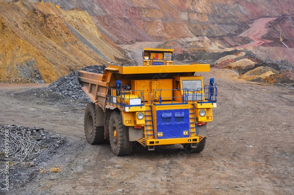 Fototapeta Extraction of iron ore. A mining dump truck transports iron ore along a side carrea. Special equipment works in a quarry