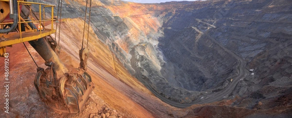 Fototapeta excavator bucket lies on the edge of the side of the iron ore quarry. Quarry panorama