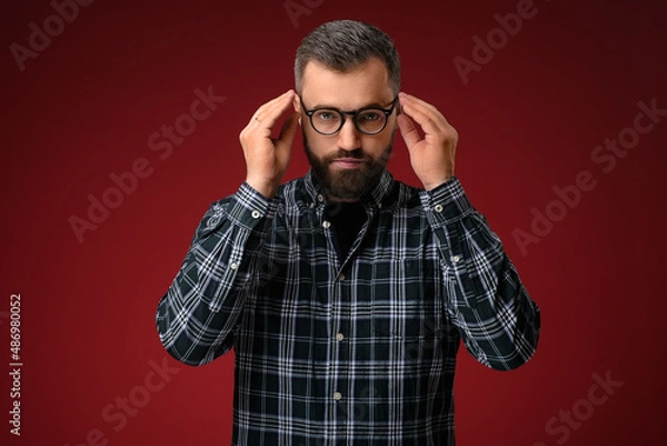Fototapeta Portrait of a cool man with a beard, holding glasses with two hands