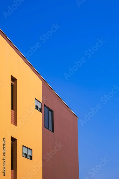 Fototapeta Side view of various fixing glass windows on orange and brown wall of modern house against blue clear sky in minimal style and vertical frame 