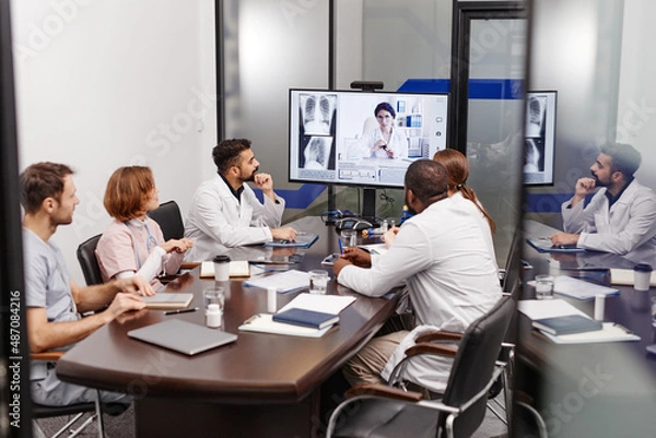 Fototapeta Large group of multi-ethnic medical experts in lab coats listening to their colleague sharing new information during online meeting