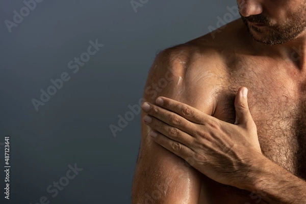 Fototapeta Close up of handsome masculine man applying cream or moisturizing body lotion onto body in bathroom. Selfcare and wellness