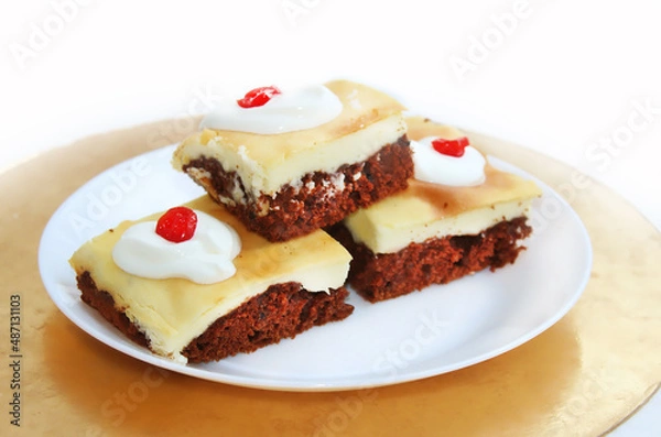 Fototapeta Cheesecake with chocolate biscuit. Pieces of cake on a white plate, sprinkled with sour cream and decorated with dried cherries
