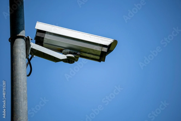 Fototapeta A security camera mounted on a metal pole during a sunny day. Blue sky in the background.