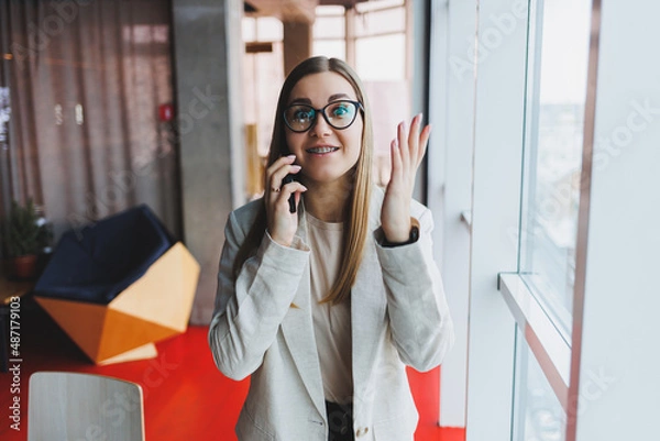 Fototapeta Young charming woman calling with a cell phone while sitting alone in a cafe in her free time, attractive woman with a sweet smile talking with a mobile phone while relaxing in a cafe
