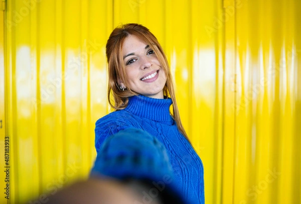 Fototapeta Selfie looking at camera of a redhead girl with blue sweater and yellow background smiling.