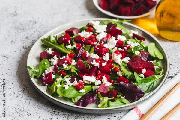 Fototapeta Arugula, Beet and cheese salad with pomegranate and dressing on plate on grey stone kitchen table background, place for text, top view