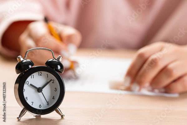 Fototapeta alarm clock with time running out. Students hands to take exams, write examination room with pencil holding on optical form of standardized test with answers 