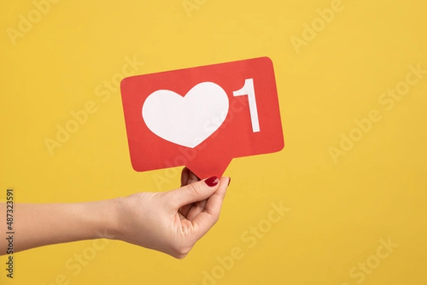 Fototapeta Support interesting web content, push heart button. Closeup of woman hand holding social media like icon, emoji sign to follow subscribe blog. Indoor studio shot isolated on yellow background.