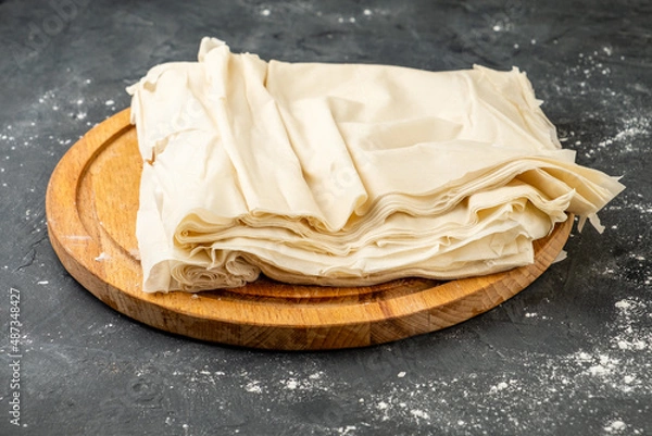 Obraz Thin filo dough for baking on a wooden board, dark table. Raw filo dough.