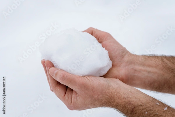Fototapeta Clasped hands of a man holding frozen snow