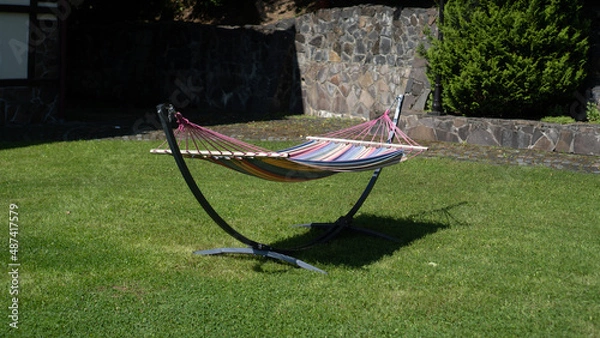 Fototapeta Colored hammock in the backyard. Fabric hammock on a metal stands in the garden. Striped fabric hammock with stand