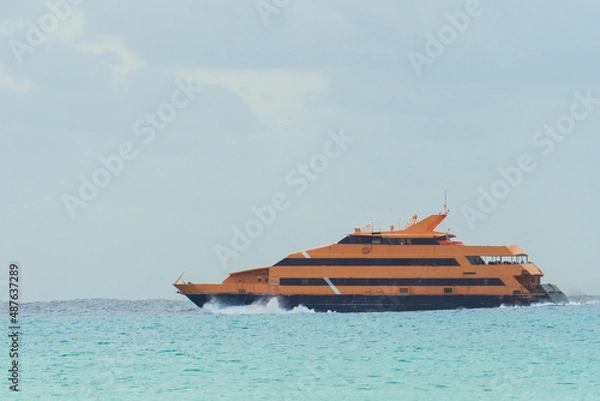 Fototapeta The liner sails on the sea against a cloudy sky. Orange yacht on the waves. Double deck ship.