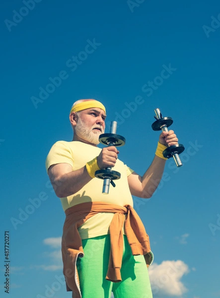 Fototapeta Health club or rehabilitation center for elderly aged pensioner. Senior sport man lifting dumbbells in sport center.