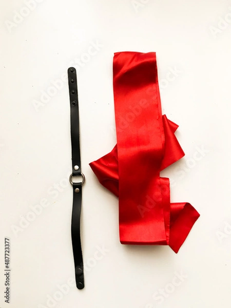 Fototapeta Red satin ribbon for binding and black leather collar, bdsm paraphernalia on a white background, top view, place for text