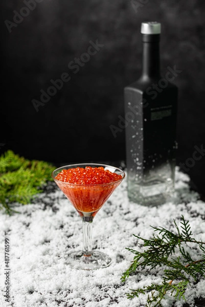Fototapeta Red salmon caviar in a martini glass on and a bottle of vodka in the snow. Copy spase