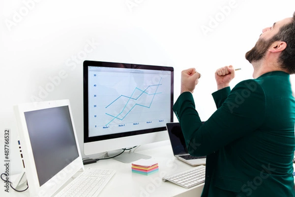 Fototapeta young man in front of the computer with pink jacket celebrating professional promotion with cheerful gesture
