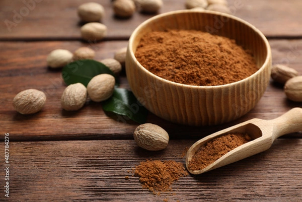 Fototapeta Nutmeg powder and seeds with green leaves on wooden table