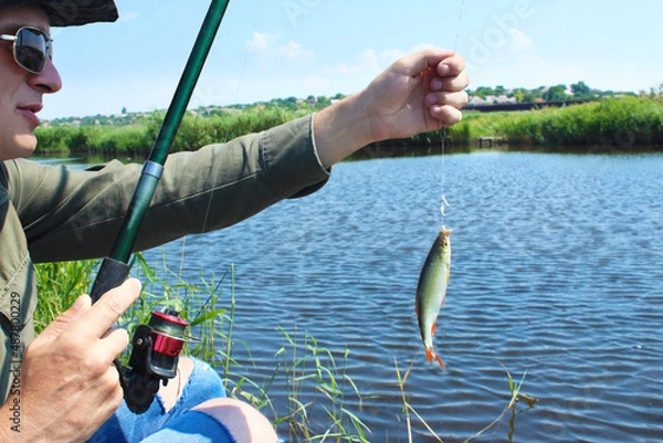 Fototapeta Caucasian young fisherman caught a fish with a bait. Catch fish on a maggot on a summer day on the river bank