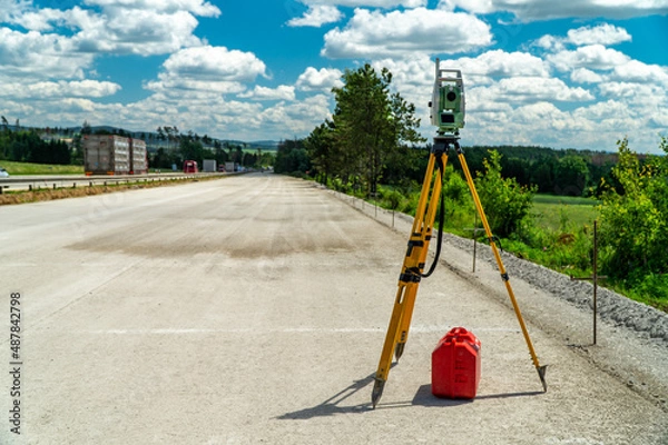 Fototapeta Surveyors equipment (theodolite or total positioning station) on the construction site of the road, highway or building with construction machinery background