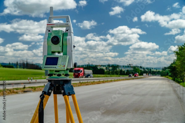Fototapeta Surveyors equipment (theodolite or total positioning station) on the construction site of the road, highway or building with construction machinery background