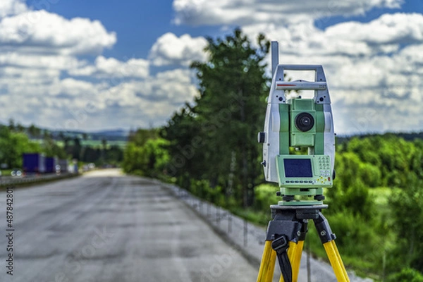 Fototapeta Surveyors equipment (theodolite or total positioning station) on the construction site of the road, highway or building with construction machinery background