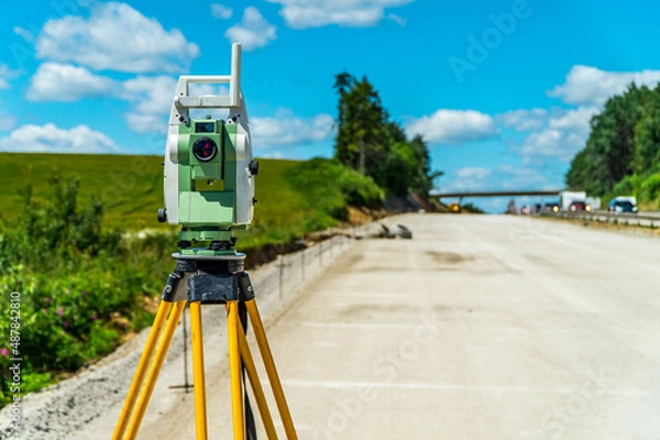 Fototapeta Surveyors equipment (theodolite or total positioning station) on the construction site of the road, highway or building with construction machinery background