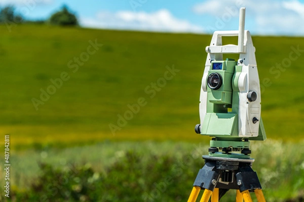 Fototapeta Surveyors equipment (theodolite or total positioning station) on the construction site of the road, highway or building with construction machinery background