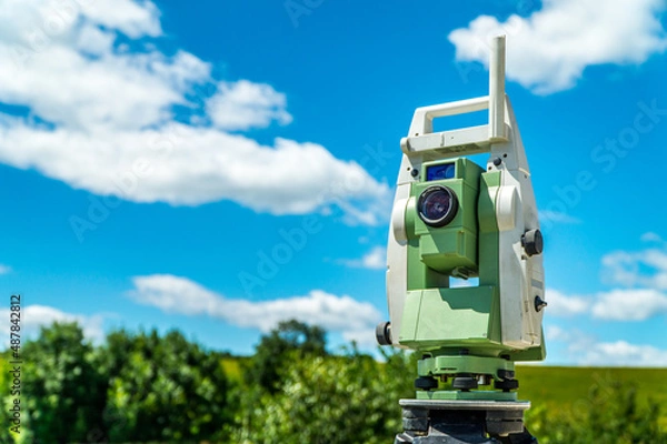 Fototapeta Surveyors equipment (theodolite or total positioning station) on the construction site of the road, highway or building with construction machinery background