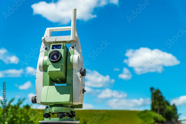 Fototapeta Surveyors equipment (theodolite or total positioning station) on the construction site of the road, highway or building with construction machinery background