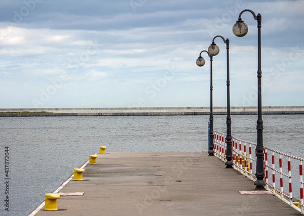 Fototapeta Empty pier in a port on a calm sea. Pier and lights at the wharf. Gentle clouds over the sea. 