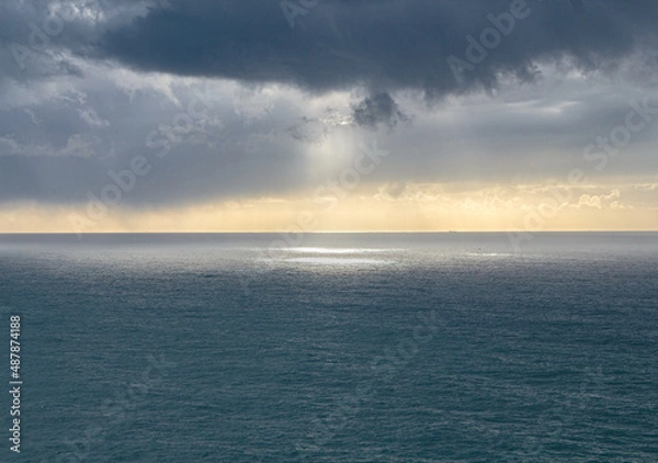 Fototapeta The sun breaking through the clouds over the ocean. Light blur in the sea. Gentle clouds over the sea. The horizon is bathed in light
