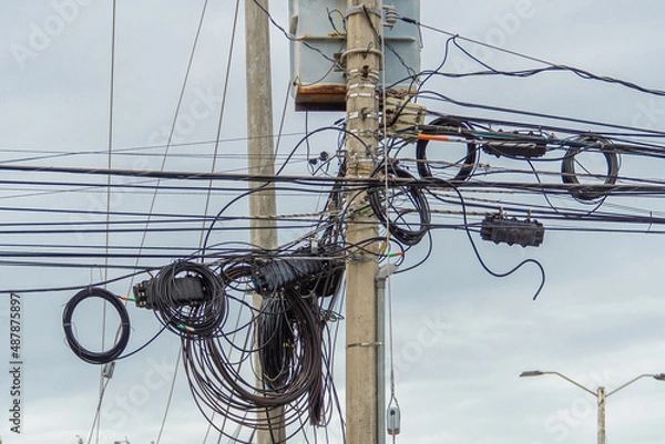 Fototapeta Chaos of cables and wires on an electric pole. Many electrical cable - wire and telephone line on electricity post. Cable breaks.