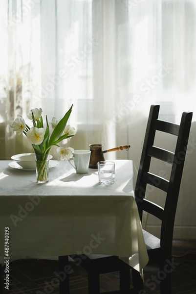 Fototapeta A bouquet of tulips on the table, white dishes, the table is covered with a white tablecloth.