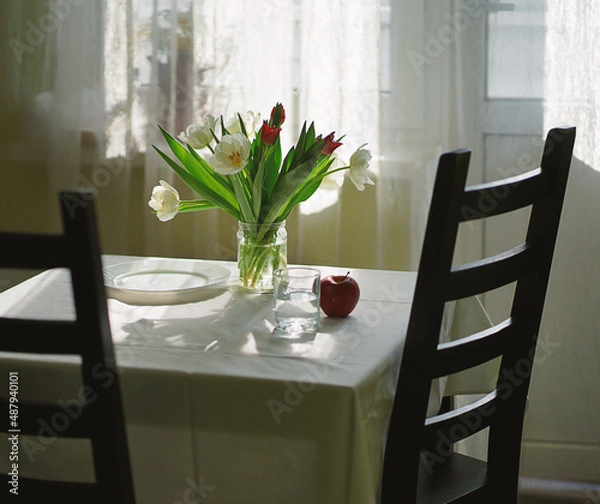 Fototapeta A bouquet of tulips on the table, white dishes, the table is covered with a white tablecloth.
