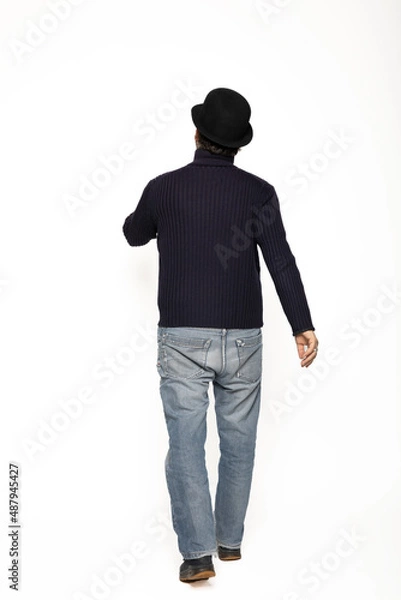 Fototapeta Man from behind walks. He is wearing a blue sweater, jeans and a bowler hat.