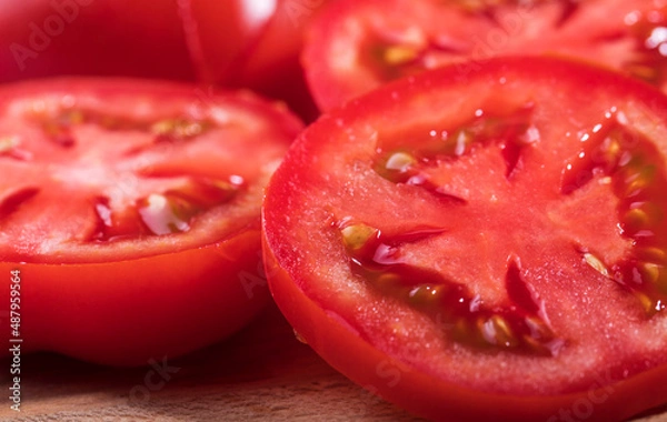 Obraz A red, ripe tomato is cut into round slices in close-up.