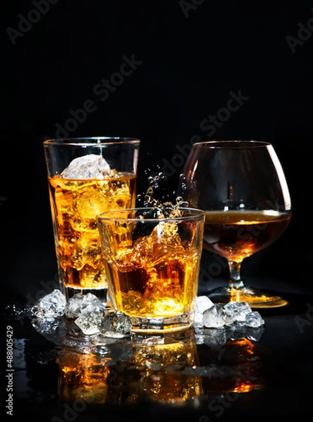 Fototapeta Three glasses of whiskey, brandy and cognac with ice cubes and drops splash