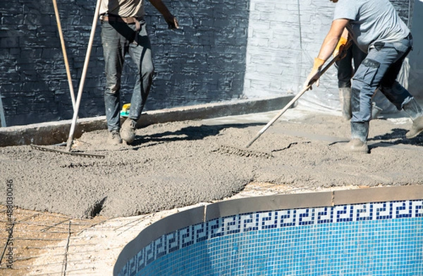 Obraz Workers distributing the concrete with rakes around the pool, fixing the garden