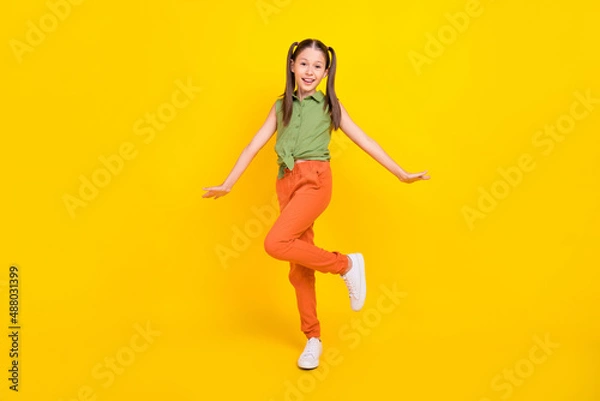 Fototapeta Photo of funny childish preteen girl dressed green top walking smiling isolated yellow color background