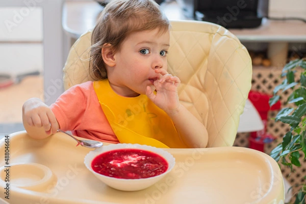 Obraz A small child eats vegetable soup with a spoon while sitting on a high chair