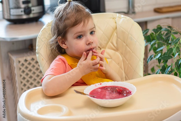 Obraz A small child eats vegetable soup with a spoon while sitting on a high chair