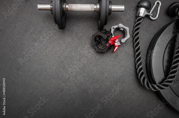 Obraz Barbell, dumbbells, triceps rope and clamps on the floor at the gym. Top down view flat lay with bodybuilding equipment on a black background and empty space for text. Fitness, weight training concept
