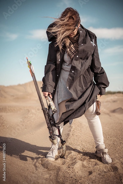 Fototapeta A girl archer in steampunk goggles and with a block bow in a post-apocalyptic image in the desert. The world after a nuclear catastrophe, survival, fantasy, the future