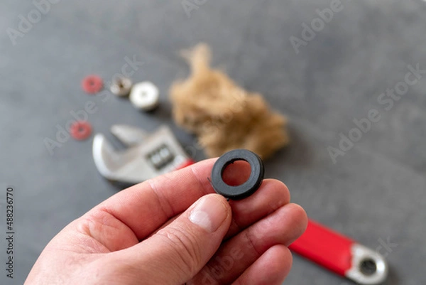 Obraz A plumber has a water seal in his hand- On the floor, there is a wrench and a plumbing linen.