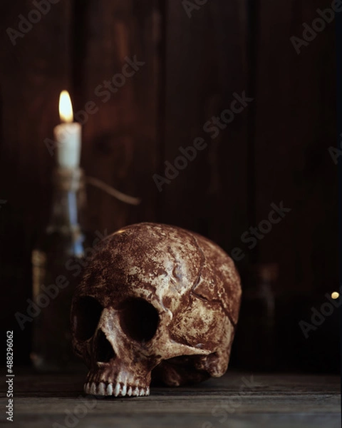 Fototapeta the skull of a man without a lower jaw stands on a wooden table with a candle