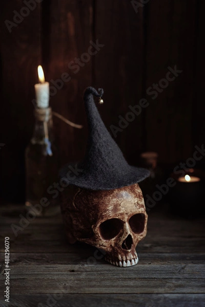 Fototapeta the skull of a man without a lower jaw in a magic hat stands on a wooden table with a candle