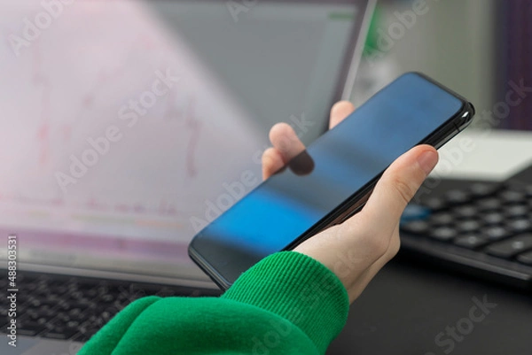 Fototapeta A falling chart on a laptop monitor and a phone in the hands of a person who is ready to sell shares.